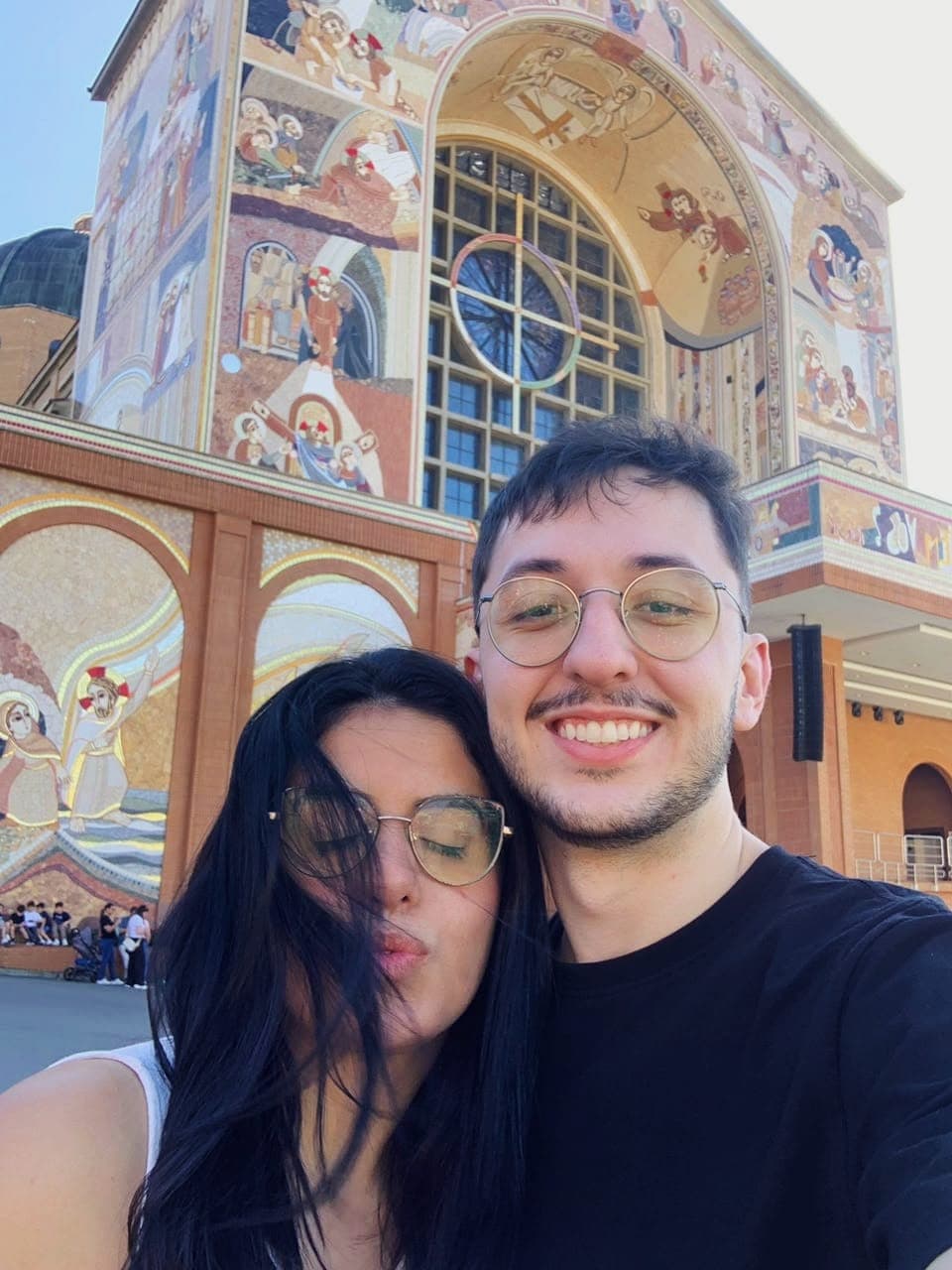 Selfie de Taíssa e Tiago diante da fachada de mosaicos da Basílica de Aparecida