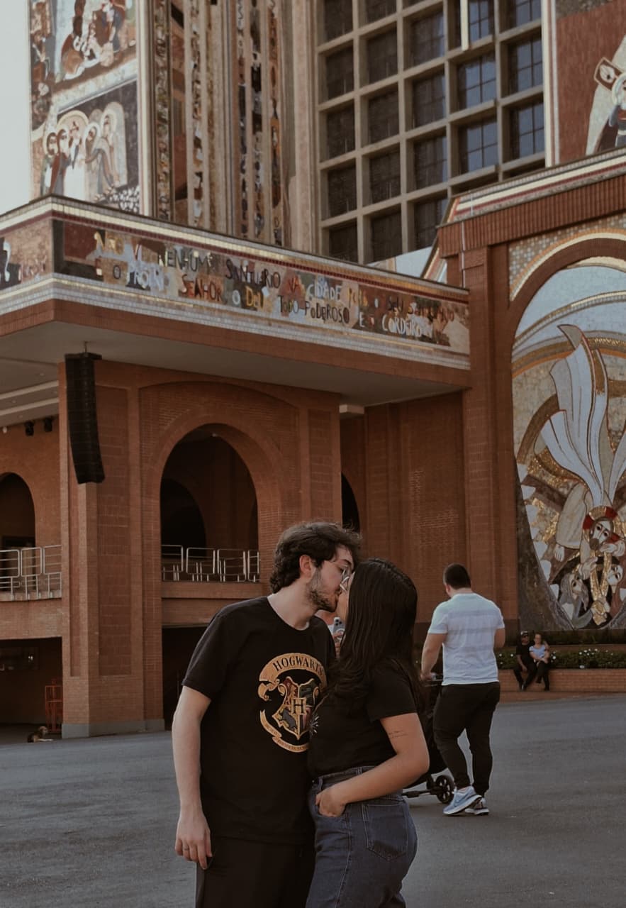 Taíssa e Tiago se beijando no pátio, com a Basílica de Aparecida ao fundo
